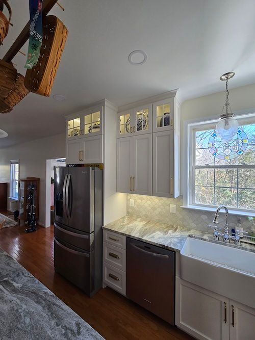 Bright kitchen with white cabinets, stainless fridge, marble backsplash, sink by window, and hardwood floor