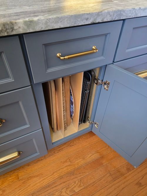 Blue kitchen cabinet with an open door revealing vertical paper storage inside