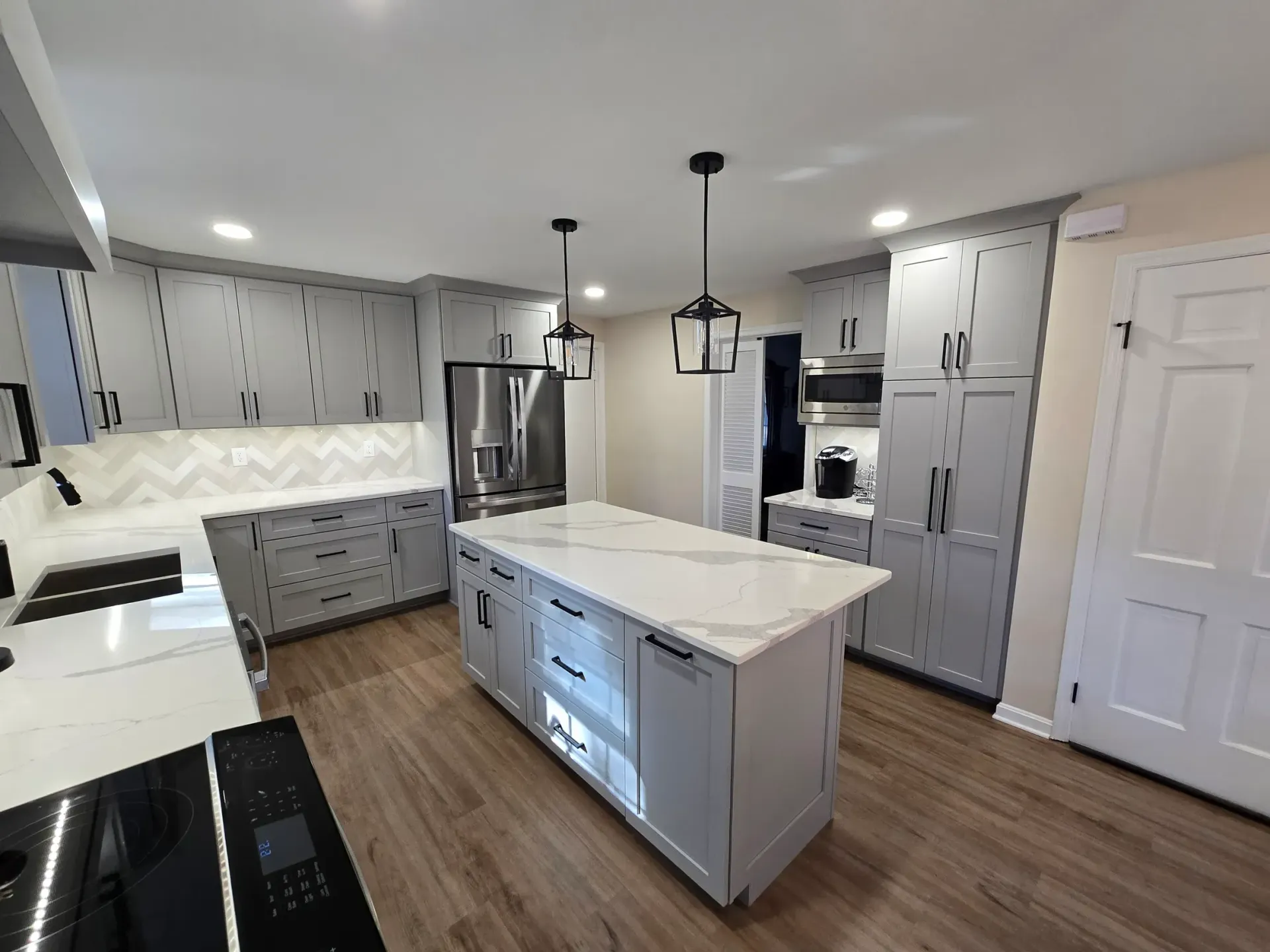Modern gray kitchen with island, white countertops, and wooden flooring.