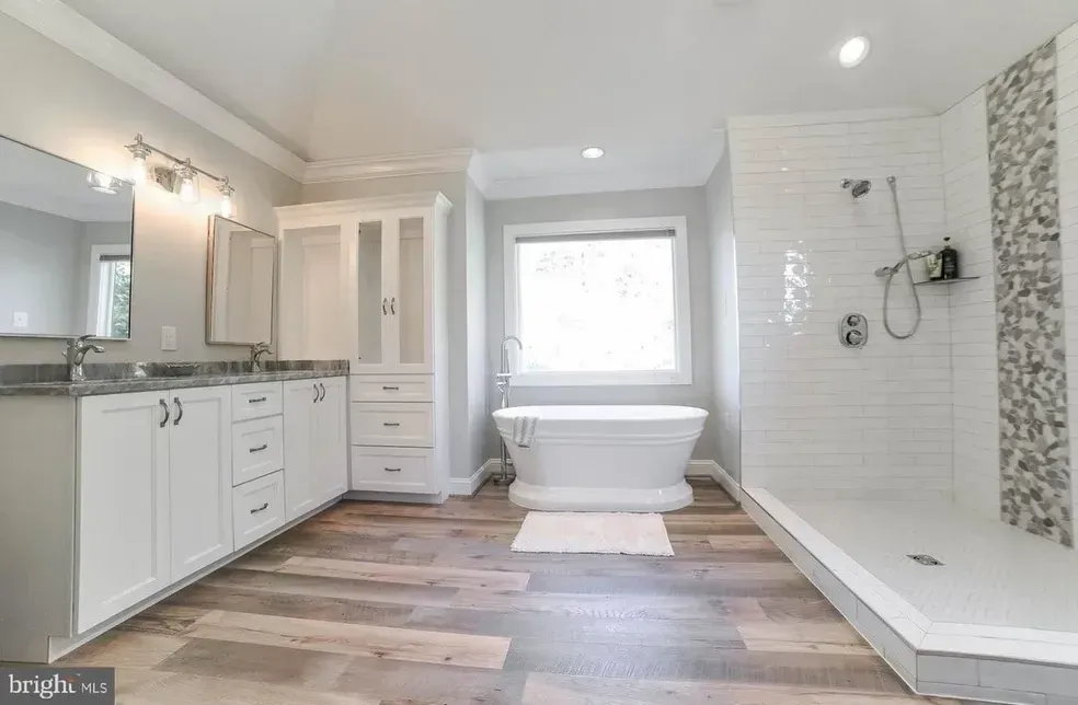 Spacious modern bathroom with a soaking tub, shower, and double vanity. Light wood-look flooring and white cabinetry.