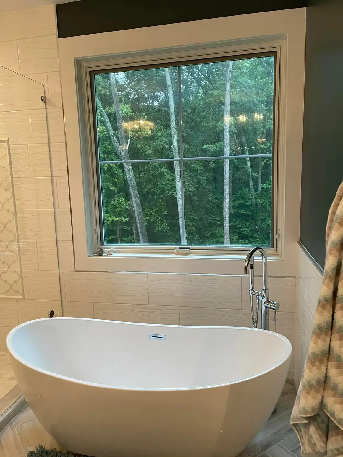 A modern bathroom with a freestanding bathtub and a window overlooking trees.