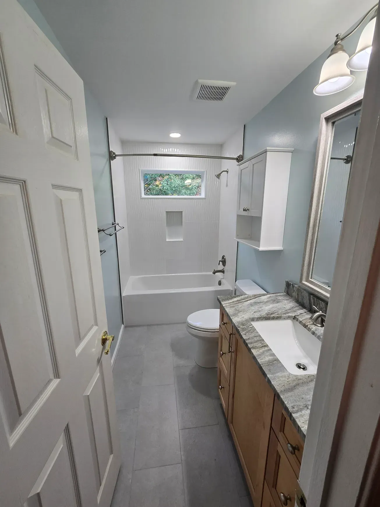 Bathroom with white tub, toilet, cabinets, and vanity with a gray countertop and blue walls.