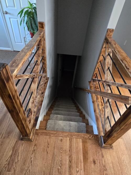 Wooden staircase descending into a dark basement between open rustic railing gates