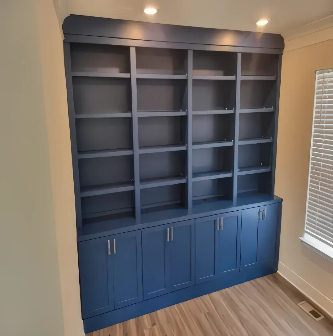 Built-in blue bookcase with cabinets and shelves, next to a window with blinds.