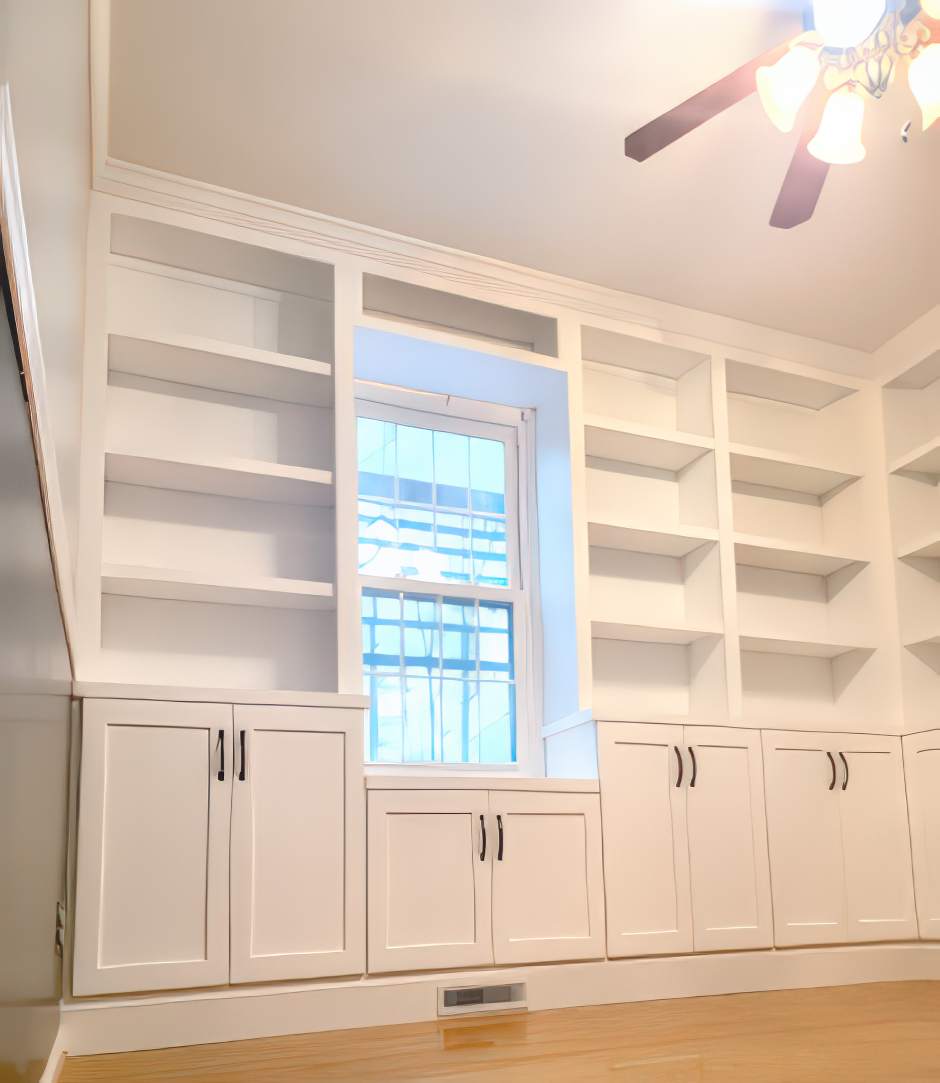 Built-in white bookshelves surround a window, with cabinets below. A ceiling fan is visible.