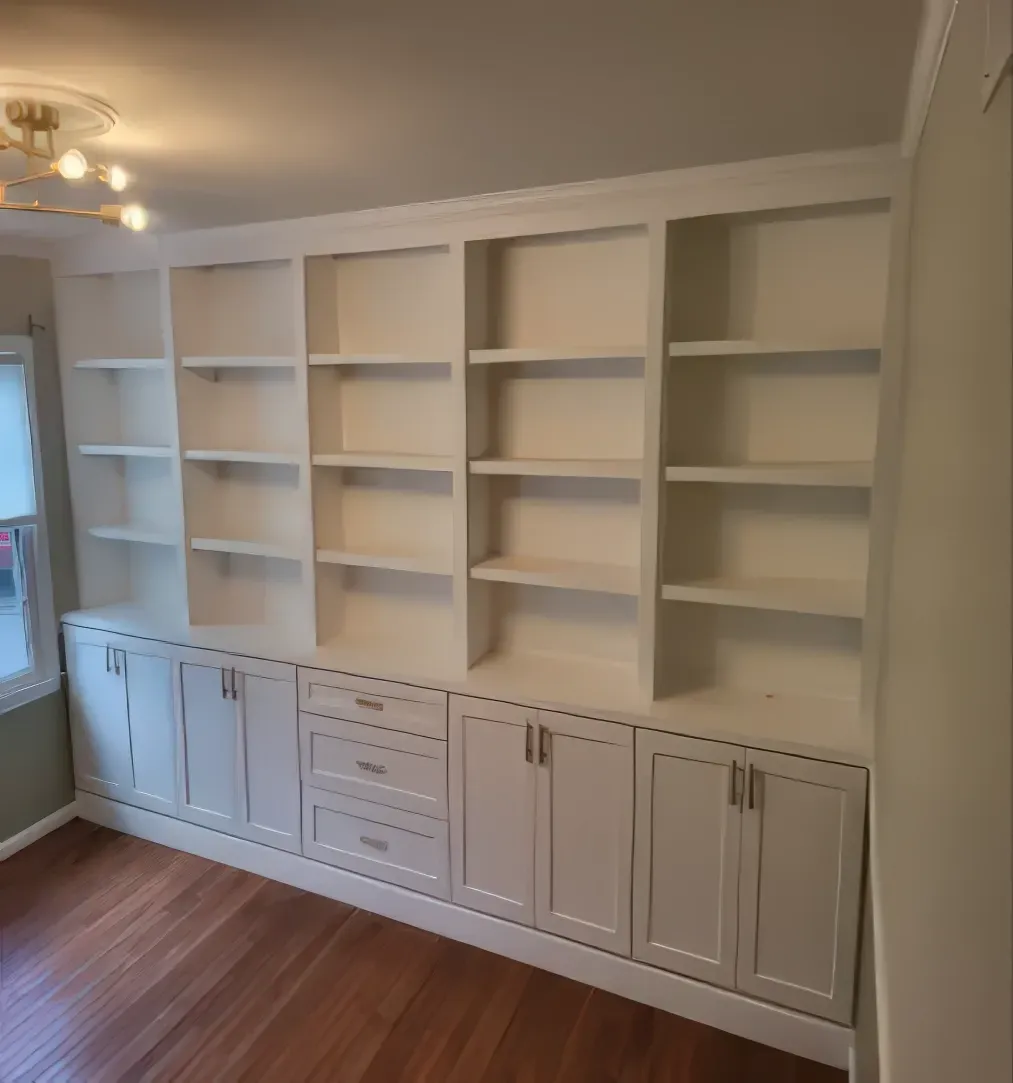 White built-in bookshelves with cabinets, drawers, and adjustable shelves against a light-colored wall.