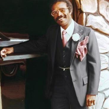 Man in a gray suit and pink tie leaning on a piano, smiling in a warmly lit room.