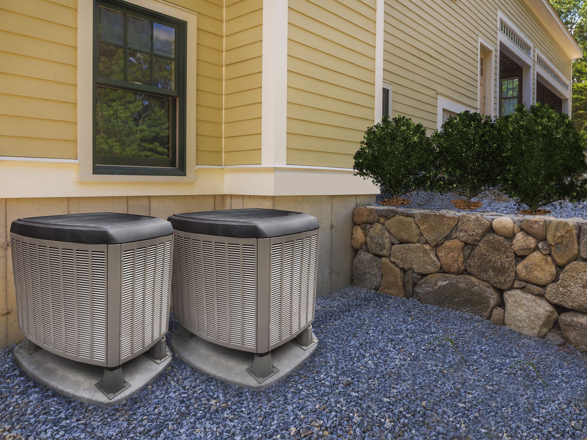 Two air conditioners are sitting on top of a pile of gravel in front of a house.