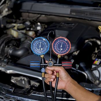 A person is holding two gauges in front of a car engine - Curry Truck & Auto