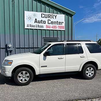 A white ford explorer is parked in front of a curry auto center - Curry Truck & Auto