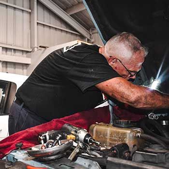 A man is working under the hood of a car in a garage - Curry Truck & Auto