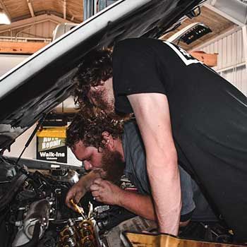 A man is working under the hood of a car in a garage - Curry Truck & Auto
