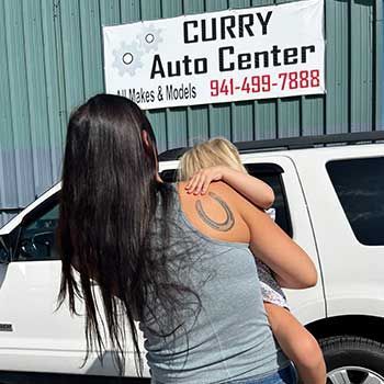 A woman is holding a child in front of a white suv - Curry Truck & Auto