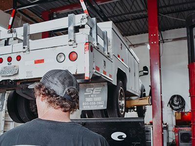 A man is looking at a truck on a lift in a garage - Curry Truck & Auto