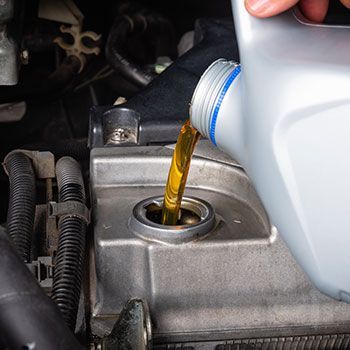 A person is pouring oil into a car engine - Curry Truck & Auto