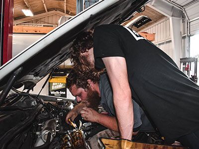 Two men are working on a car engine in a garage - Curry Truck & Auto