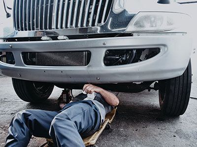 A man is laying on a jack under a truck - Curry Truck & Auto