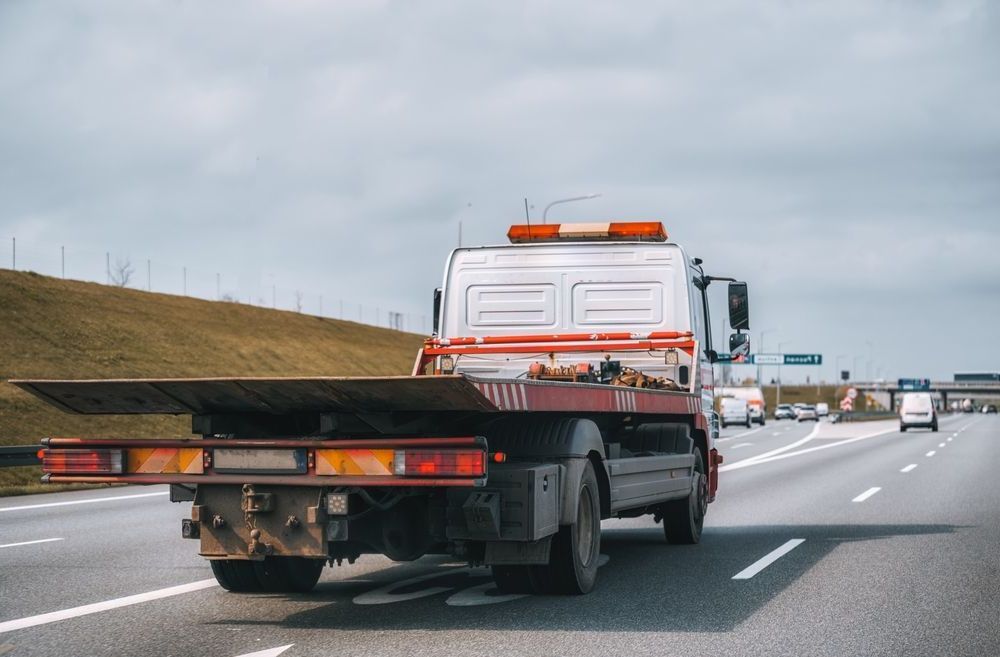 A Tow Truck With A Flat Bed Is Driving Down A Highway — Torquay & Anglesea Accident Towing Centre In Anglesea, VIC