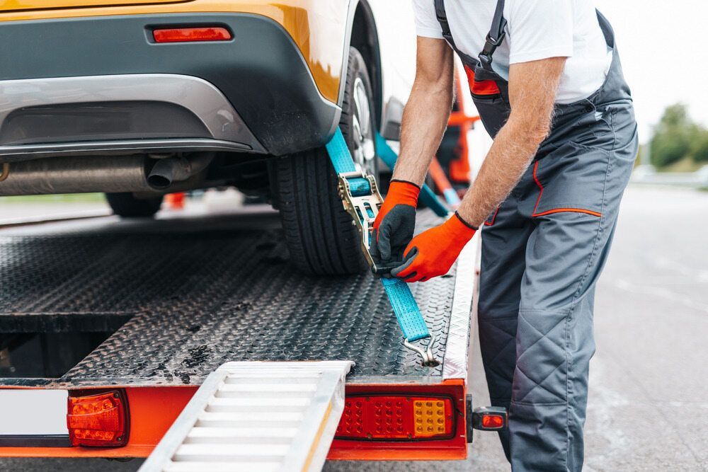 A Man Is Tying A Car To A Tow Truck — Torquay & Anglesea Accident Towing Centre In Anglesea, VIC 