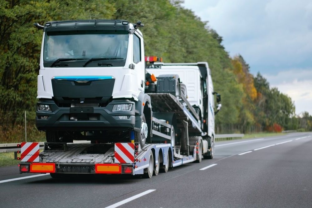 A Truck Is Driving Down A Highway With A Car On The Back Of It — Torquay & Anglesea Accident Towing Centre In Otways, VIC