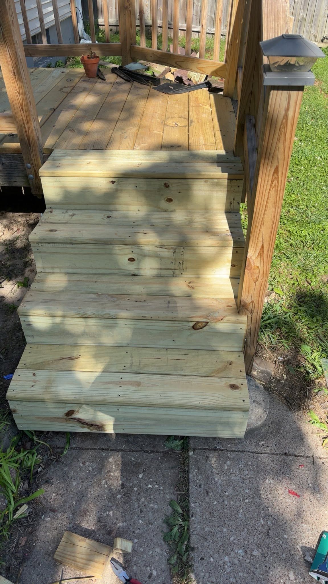 Wooden ramp leading to a raised porch with railings and deck lights beside a grassy yard