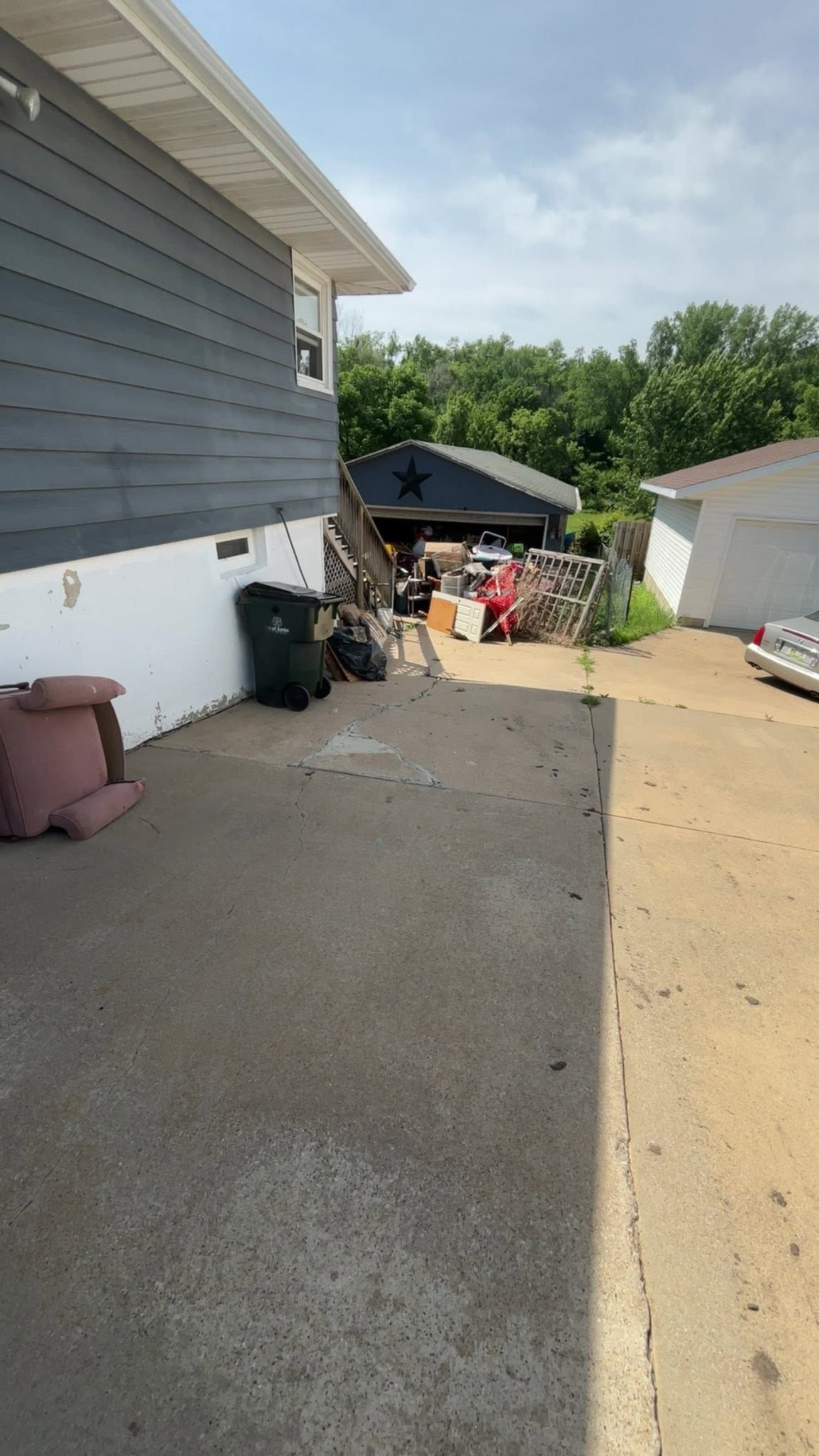 Narrow side yard beside a gray house, with gravel, stored items, and a shed at the end.