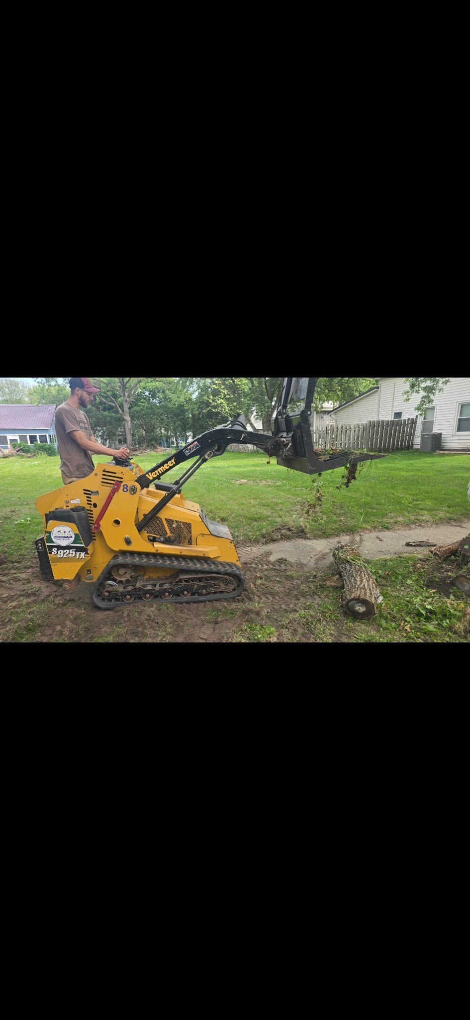 Yellow mini excavator digging dirt beside a grassy yard and house