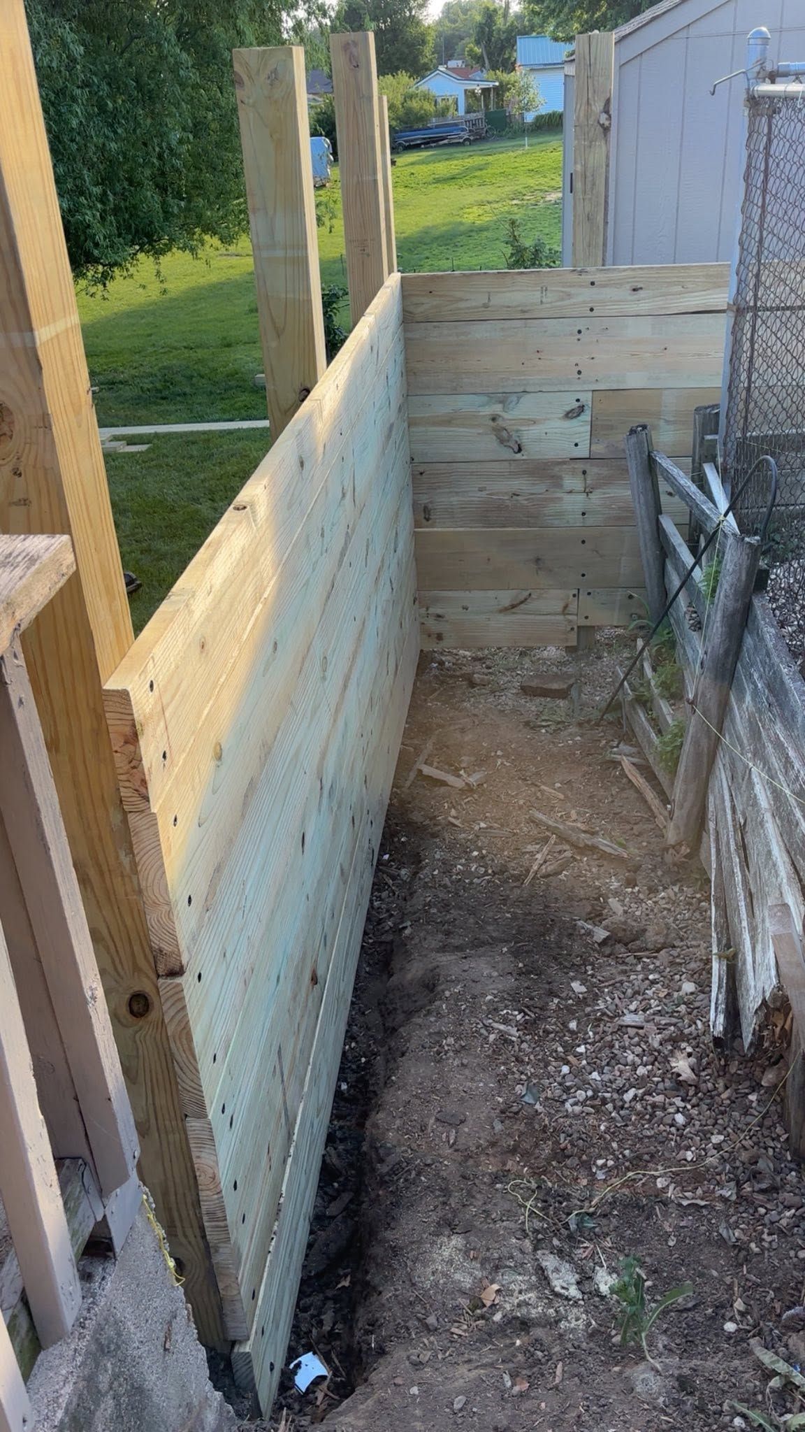 Narrow fenced wooden ramp under construction beside a shed, with posts and gravel path.