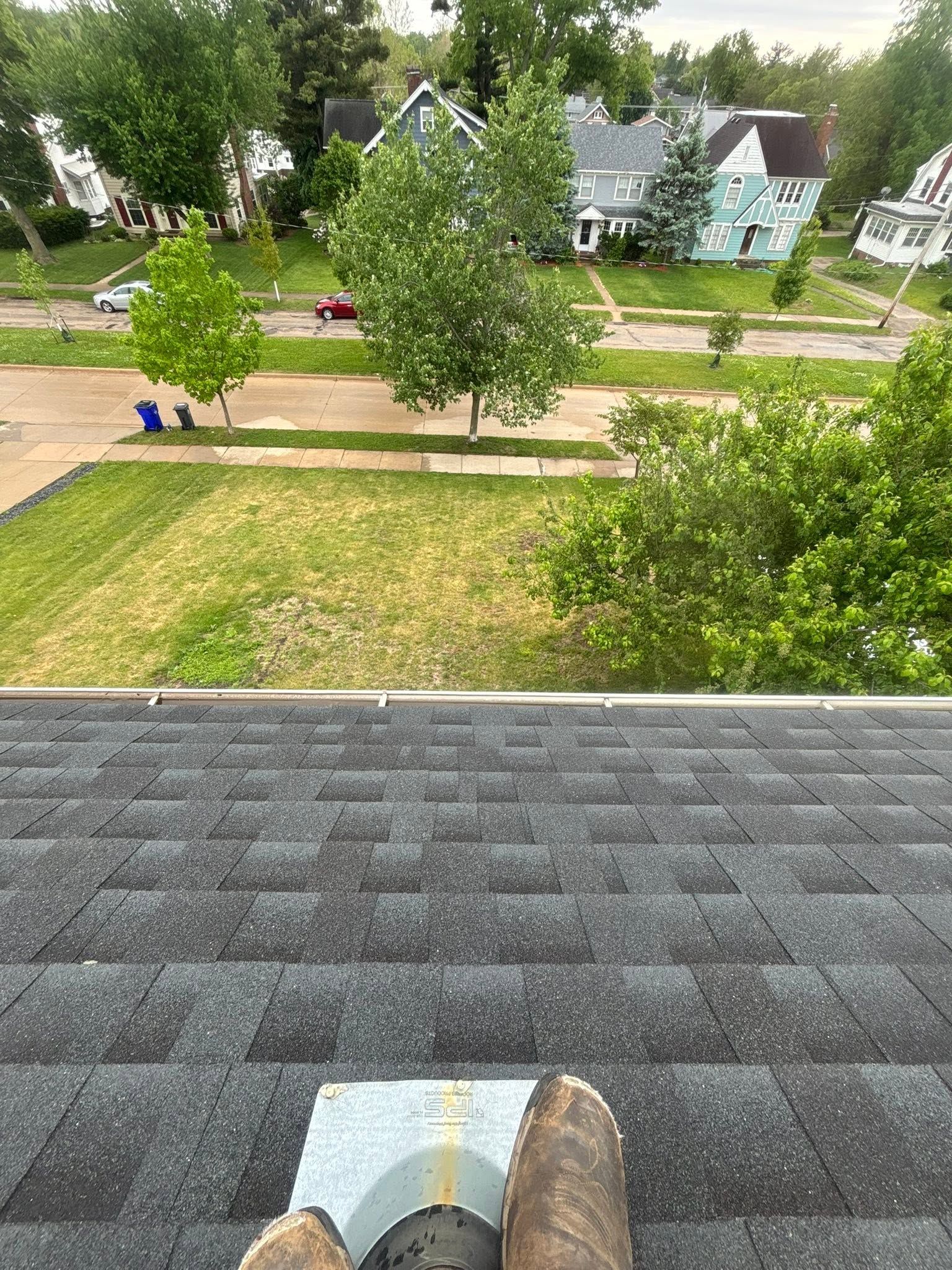 View from a rooftop over a leafy neighborhood street and houses, with a boot visible at the bottom edge