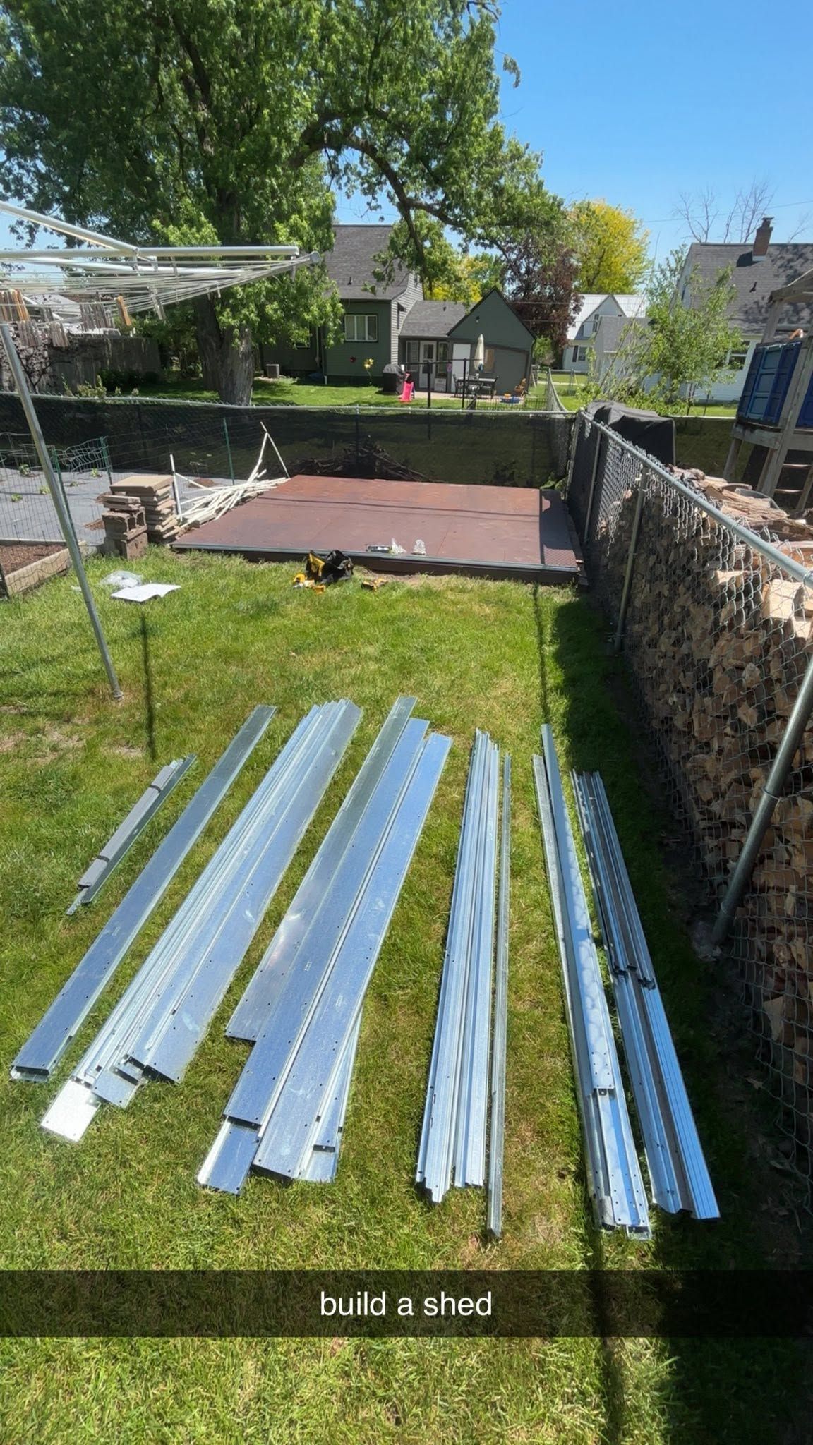 Metal roofing panels laid on a grassy backyard beside a raised deck and fence