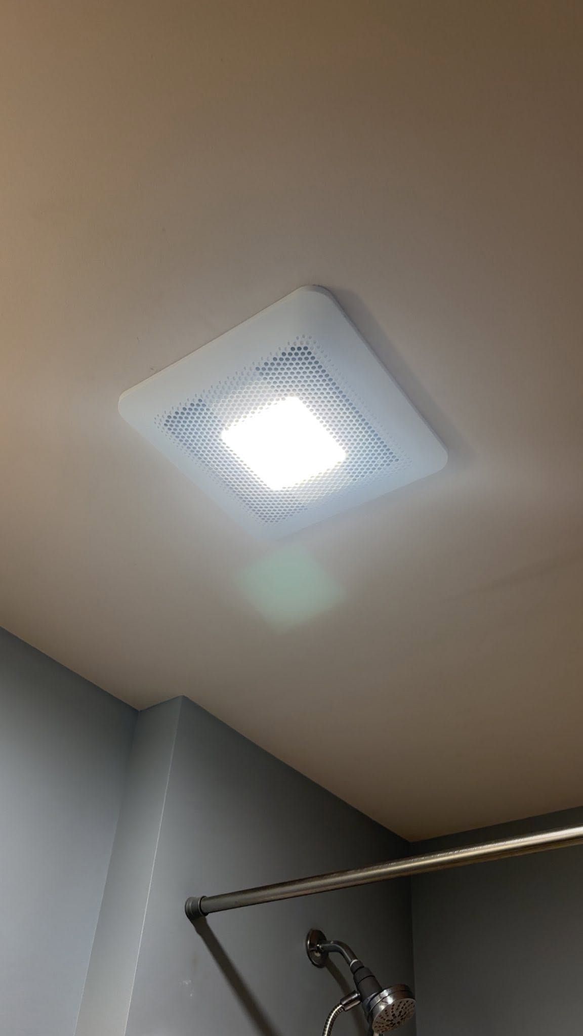 Ceiling light on a beige bathroom ceiling above a shower curtain rod