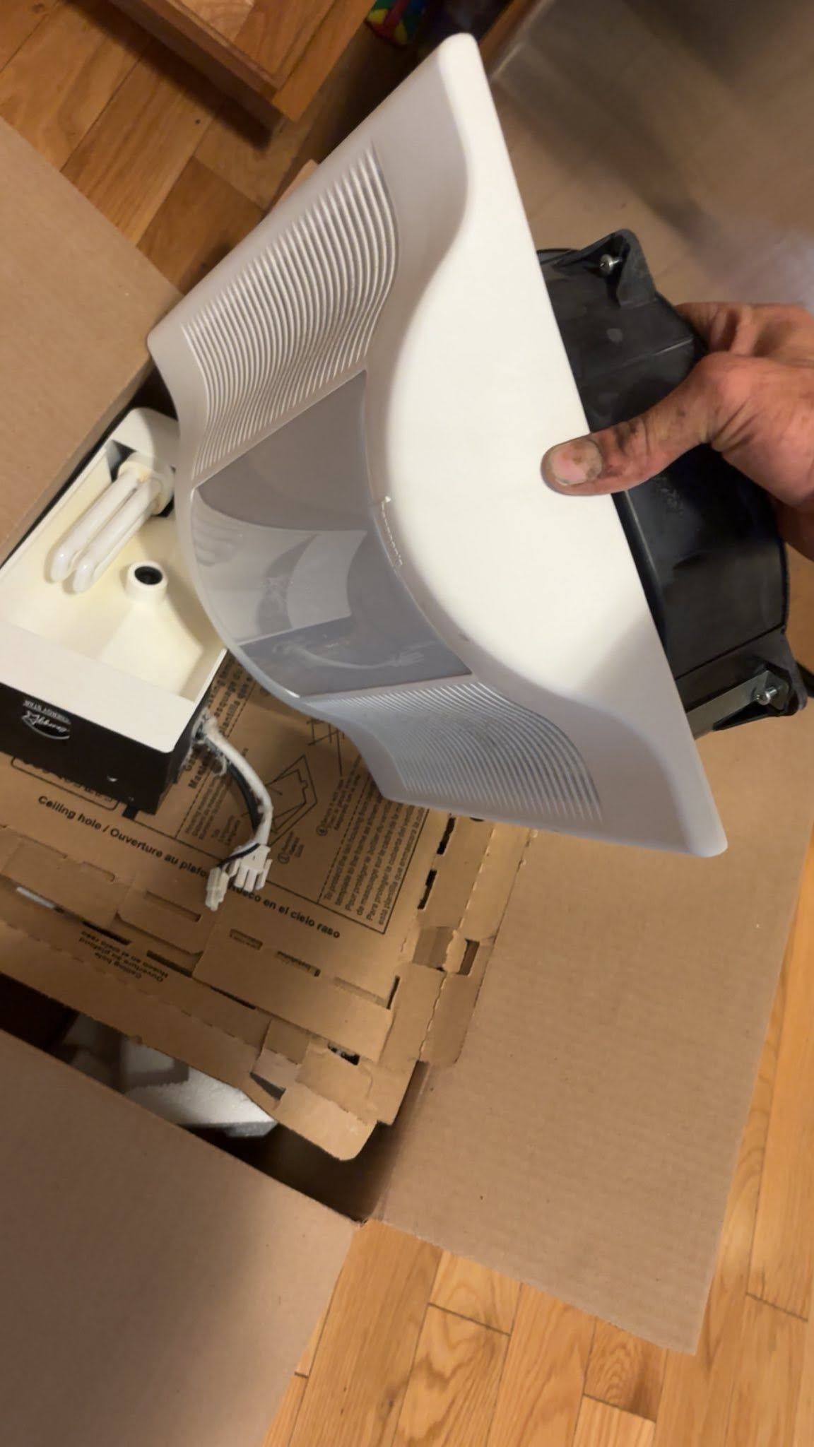 Hand holding a white vented electronic device over a cardboard box and packaging materials