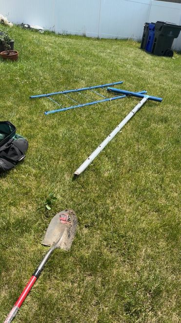 Lawn with scattered garden tools: blue and white poles, a red-handled net, and a small bag near a fence.