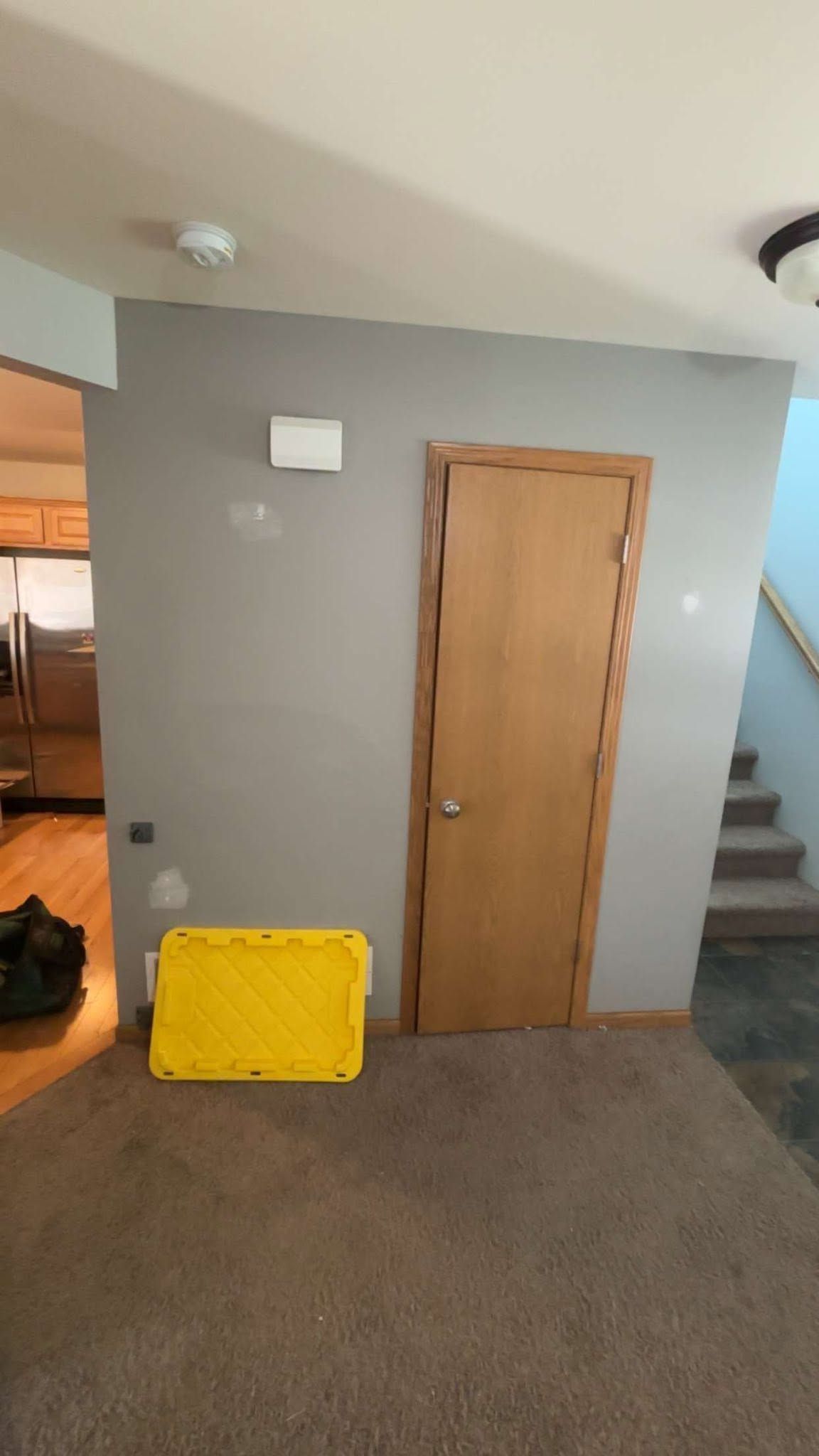 Indoor hallway with a wooden door, stairs, and a yellow folded barrier against a gray wall.