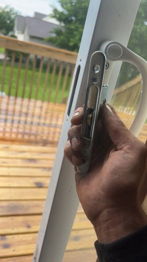 Hand holding a smartphone and a round metal keyring near a white railing, with a wooden deck outside.