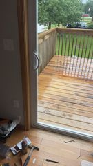 Open doorway to a wet wooden deck with railing and yard outside; small object on floor inside.