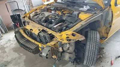 A yellow car with the hood open is sitting in a garage.