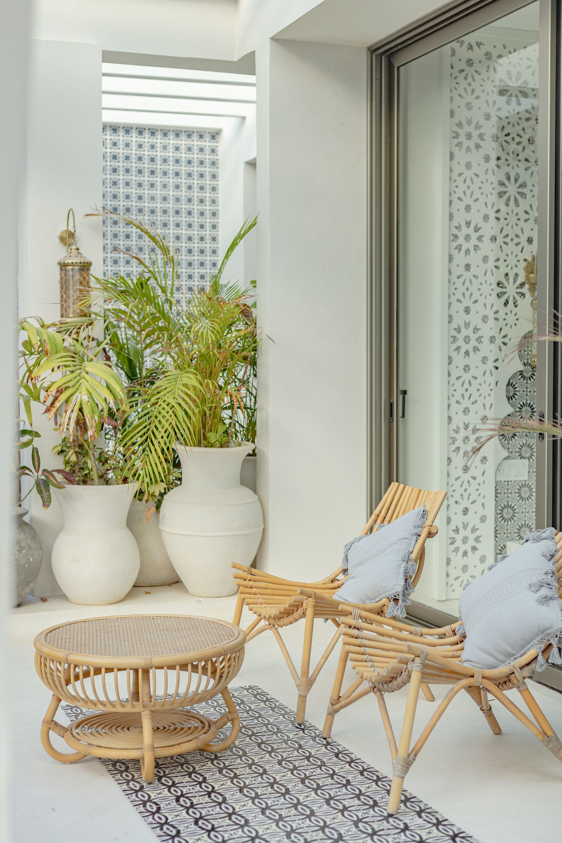 Outdoor seating area with rattan furniture, white walls, and potted plants.