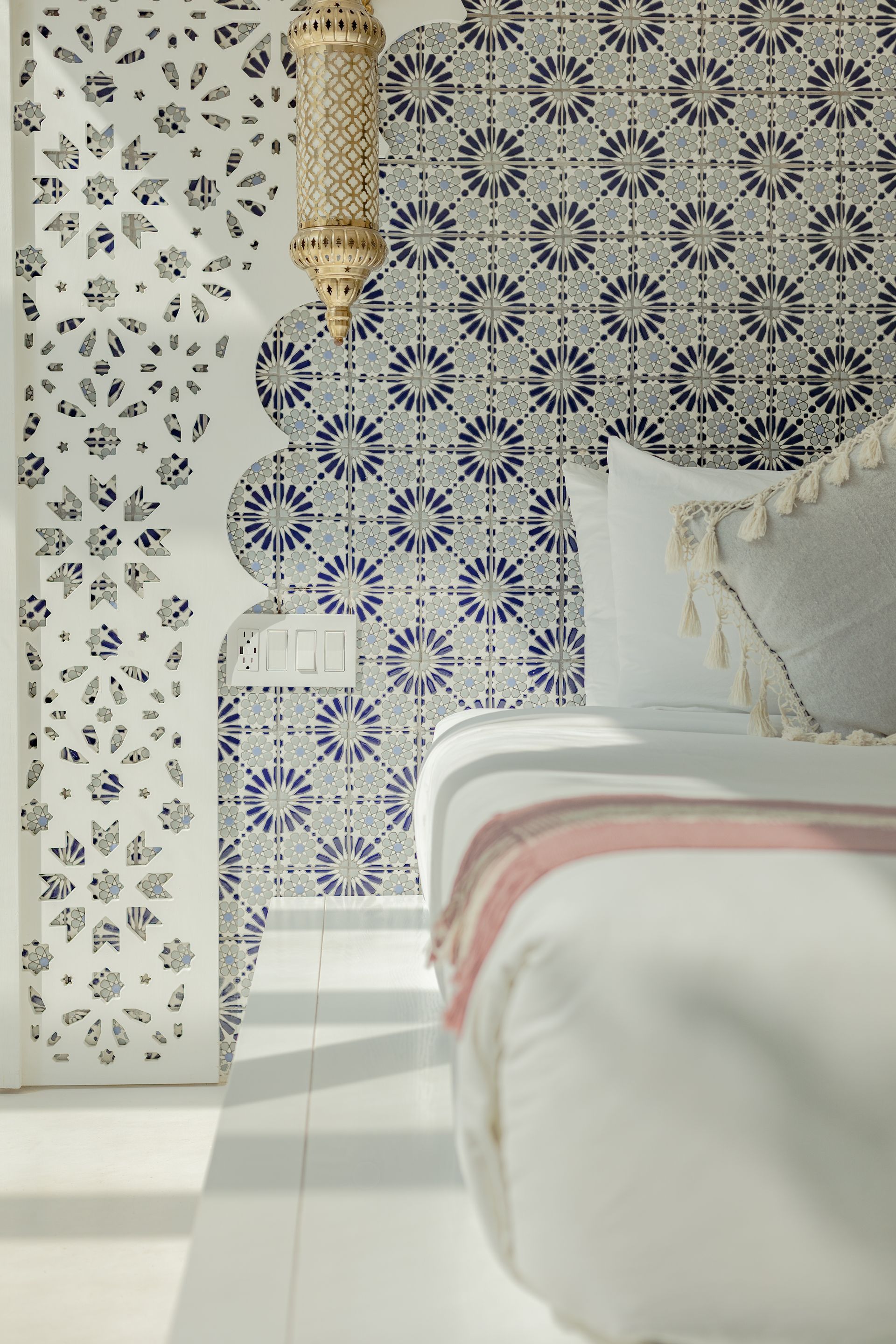 Dormitorio con pared de azulejos estampados en azul y blanco, molduras decorativas blancas y una cama blanca con una manta de color claro.