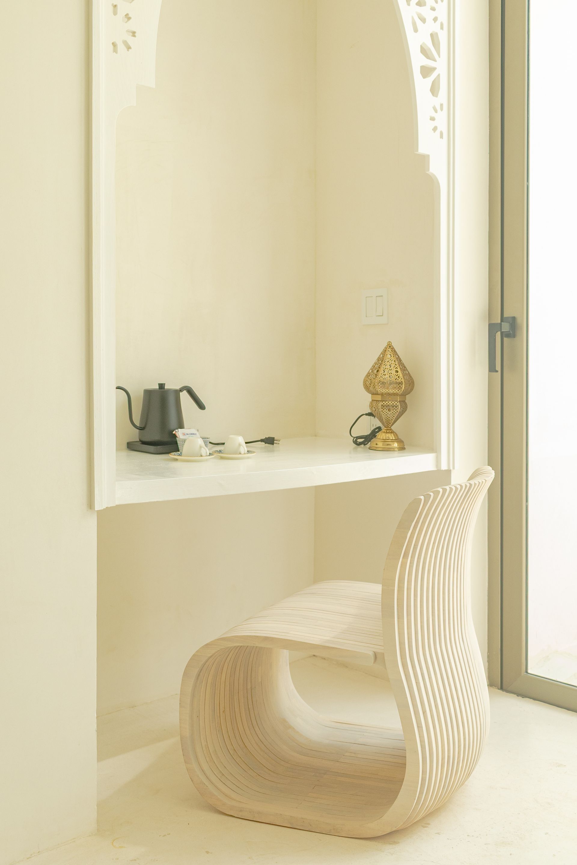 Escritorio empotrado con silla. Estante con tetera, tazas y escultura dorada. Habitación blanca con detalle de arco 