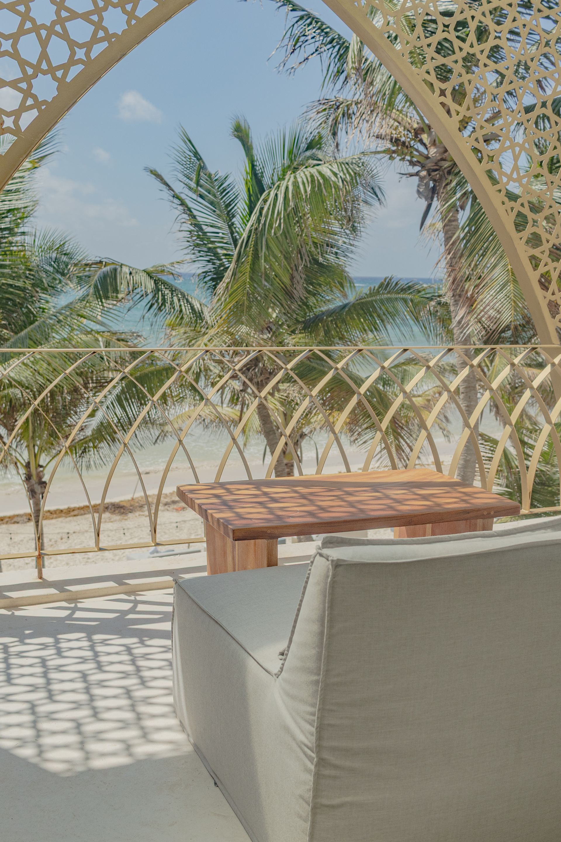 Zona de estar beige con mesa de madera, abierta a la playa y palmeras.
