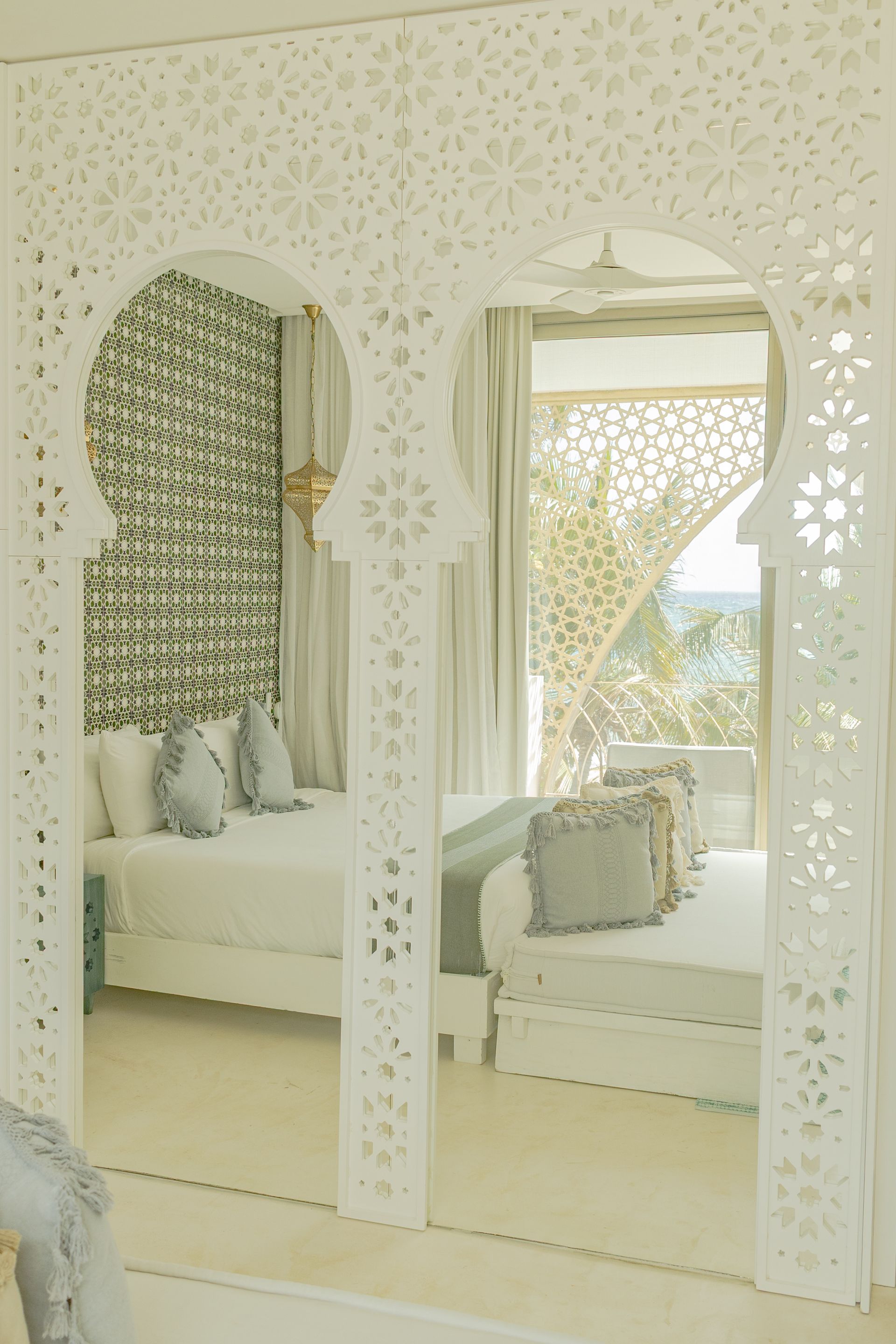 Interior de dormitorio con una puerta blanca y ornamentada en forma de arco. Contiene una cama con almohadas y paredes estampadas.