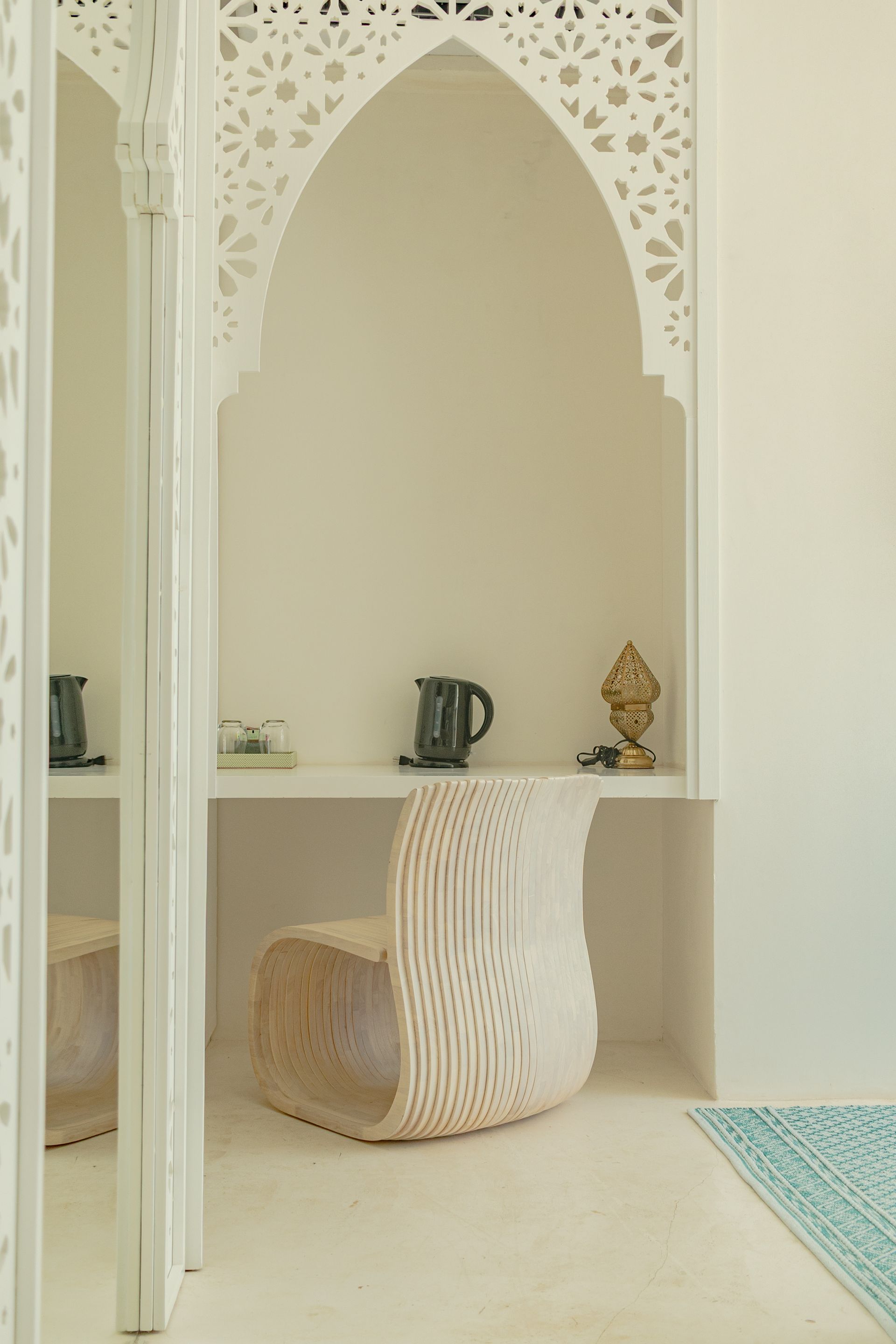 Escritorio empotrado blanco con arco decorativo y silla elaborada. Tetera negra y estatua dorada en el estante.