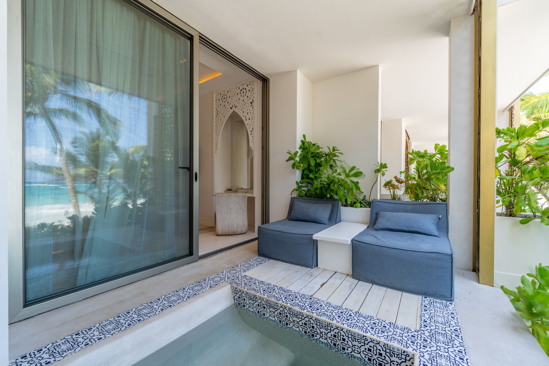 Outdoor lounge area with blue seating, a small pool, and beach view.