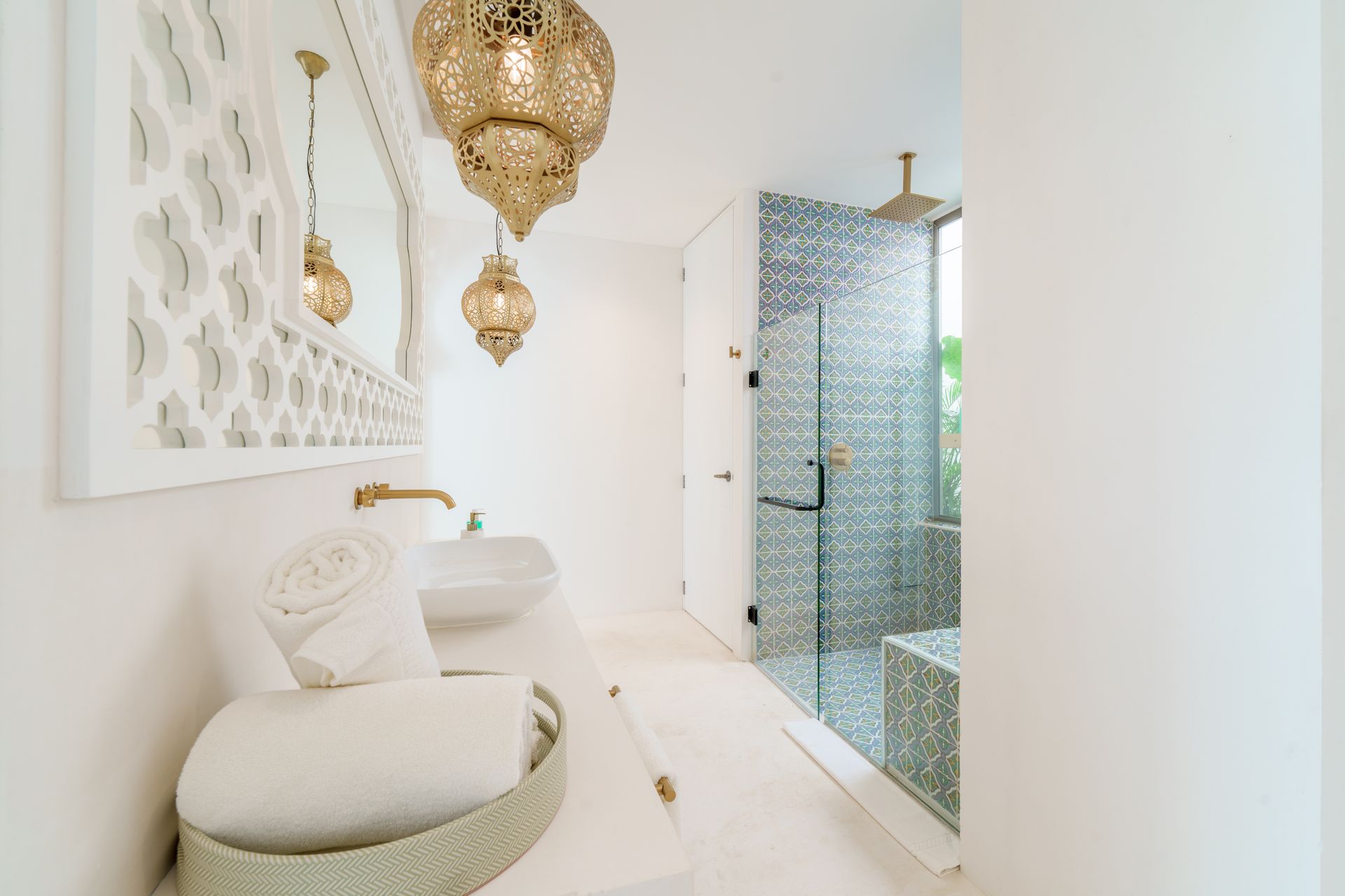 Elegante baño blanco con detalles dorados. Incluye ducha de mosaico, faroles ornamentados y toallas de felpa.
