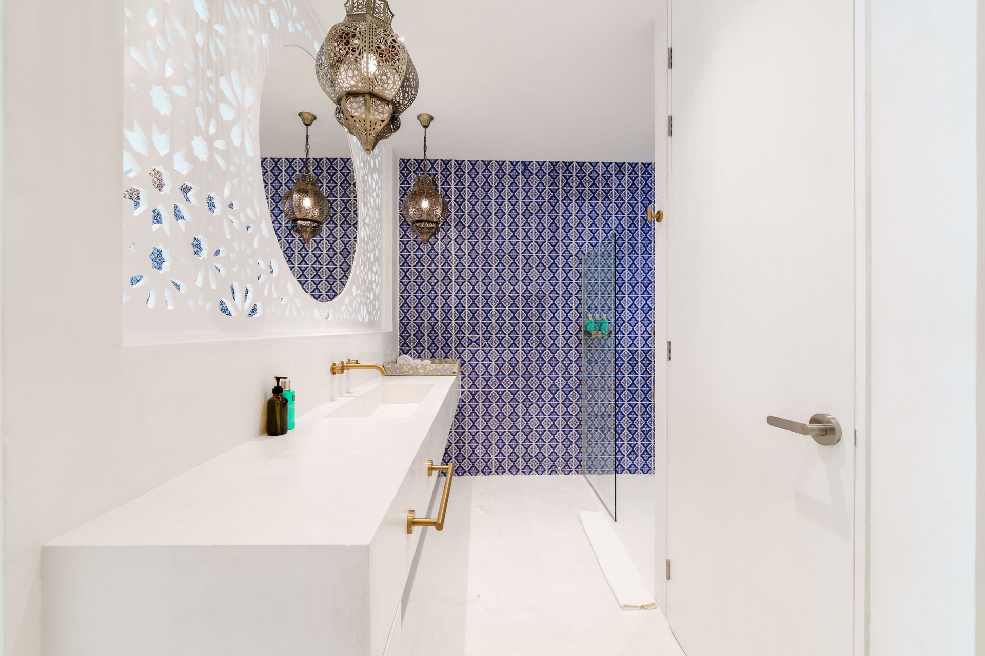 Bathroom with white countertops, blue tile wall, ornate gold light fixtures, and a decorative mirror.