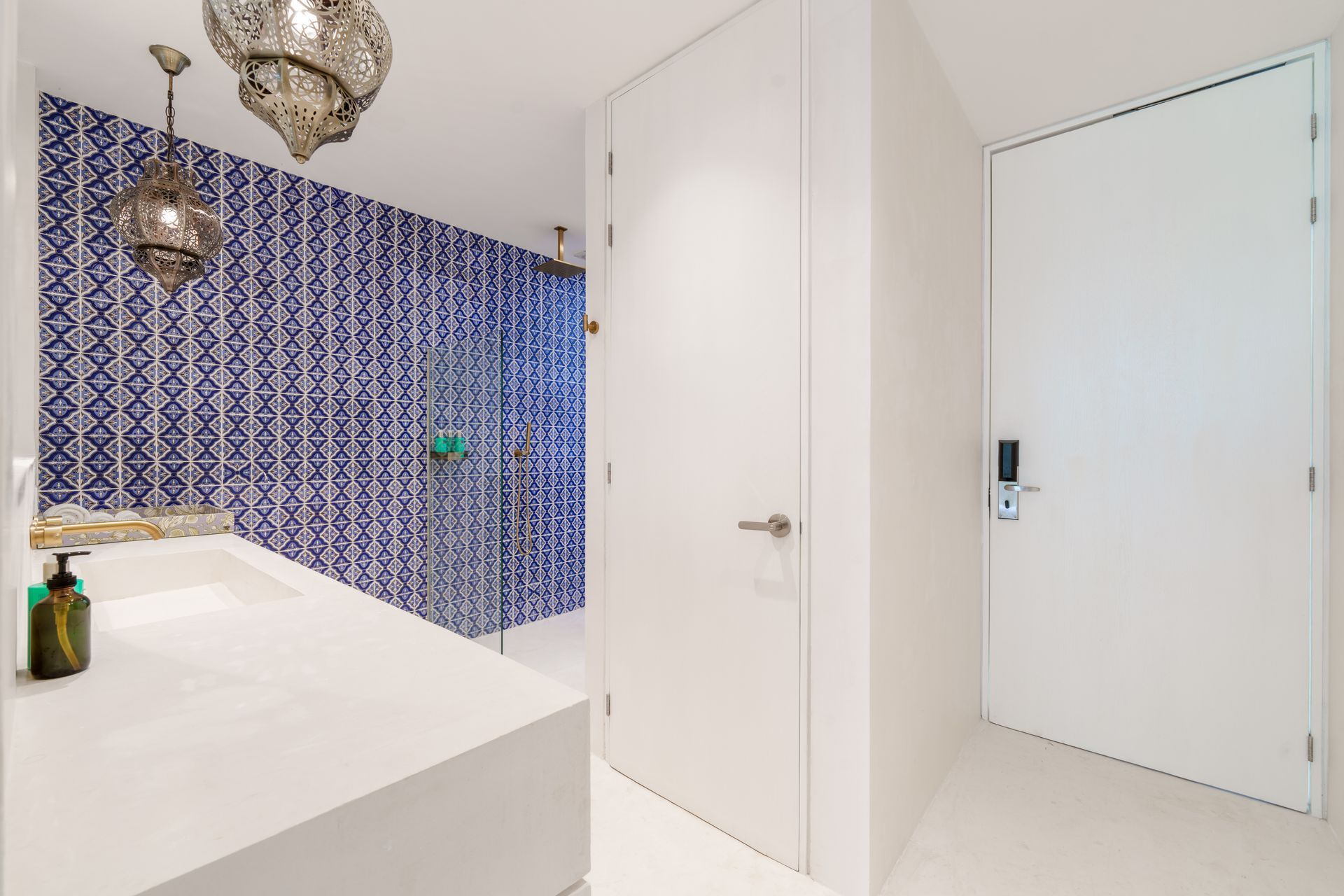 Baño con azulejos azules y blancos, lavabo blanco y puertas blancas.