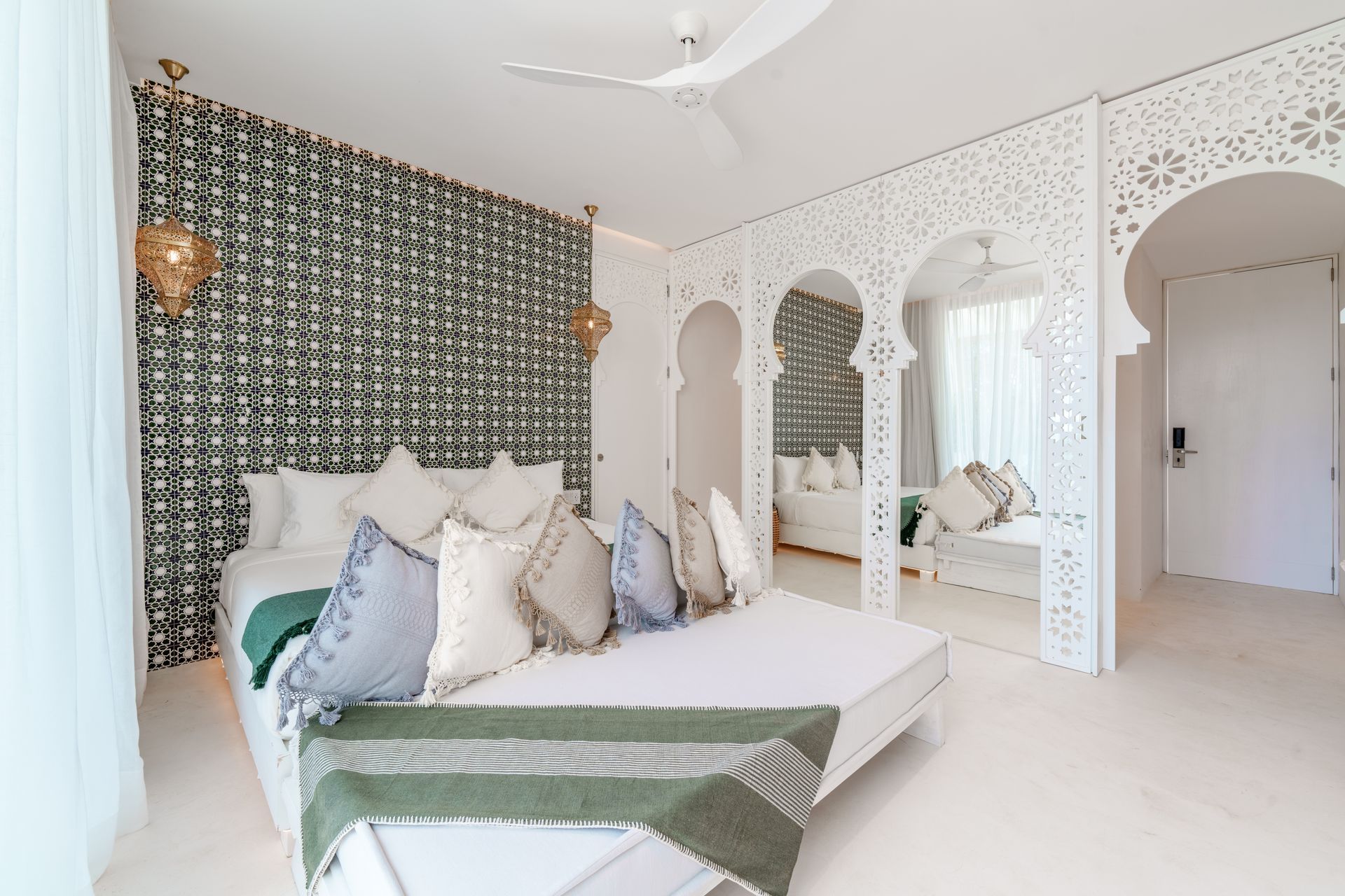 Dormitorio con arcos blancos tallados, pared estampada, cama con almohadas decorativas y zona de estar.