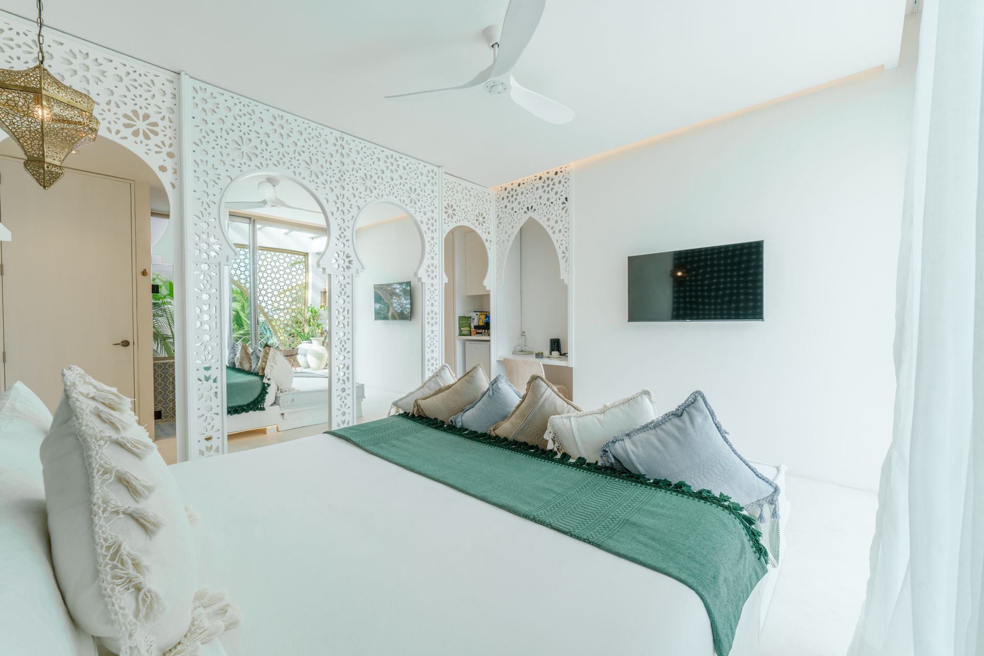 Dormitorio blanco con arco , cama tamaño king con camino de mesa color verde azulado, almohadones y tv en la pared.