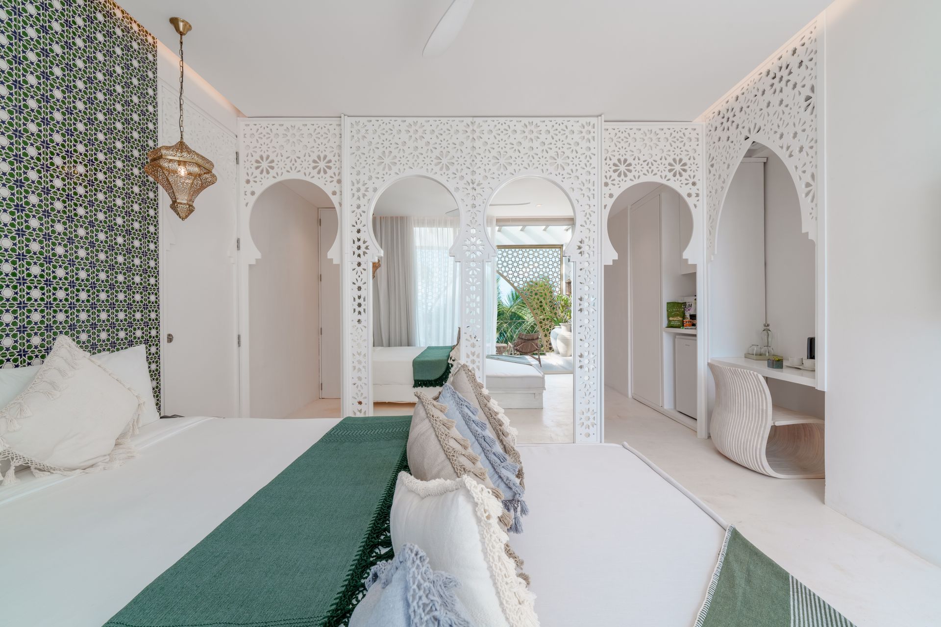Dormitorio con arcos blancos ornamentados, detalles en verde azulado y vista a un patio.